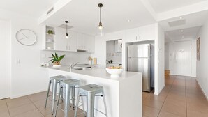 A modern kitchen with white cabinetry, a central island with stools, a stainless steel refrigerator, and pendant lighting.