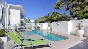 A modern pool area with lounge chairs, a clear pool, and a white building with balconies.