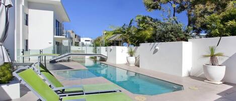 A modern pool area with lounge chairs, a clear pool, and a white building with balconies.