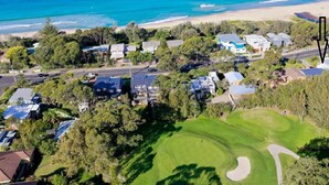 An aerial view of a coastal residential area with houses, a golf course, and a beach. - Surfrider | Bright Beachfront Apartment | Mollymook Beach (Mollymook Beach)