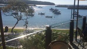 A terrace with a view of boats on water, a table, chairs, and umbrellas. - Surfrider | Bright Beachfront Apartment | Mollymook Beach (Mollymook Beach)