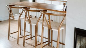 A modern kitchen with white cabinets, a wooden dining table, and bar stools. - The Cedar- Waterfront /SAUNA /Kayaks /Swimming (Cape Breton Regional Municipality)