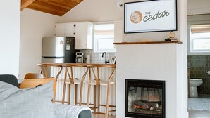 A modern living room with a fireplace, wooden ceiling beams, a dining area, and a kitchen. - The Cedar- Waterfront /SAUNA /Kayaks /Swimming (Cape Breton Regional Municipality)