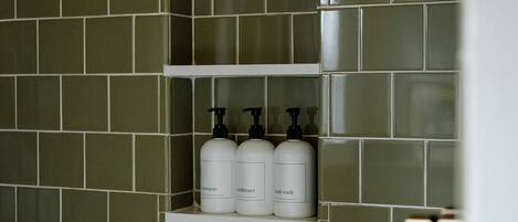 A bathroom with green tiles, a shelf with three bottles of shampoo, conditioner, and body wash.