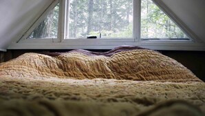 Un dormitorio con un ventanal grande, una cama con un edredón texturizado y vistas a árboles.