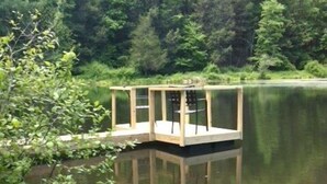 Un muelle de madera con una silla y una mesa, rodeado de agua y vegetación.