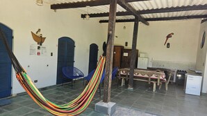 Une pièce avec un hamac, des chaises bleues, une table en bois et un réfrigérateur.