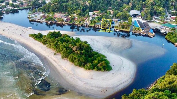 Vue aérienne d’une zone côtière avec une plage de sable en forme de courbe, une petite île couverte d’une végétation luxuriante et un quai où sont amarrés des bateaux.