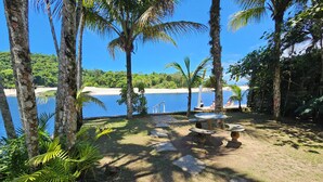 Un espace extérieur de style tropical, avec une table et des bancs en pierre, entouré de palmiers et offrant une vue sur une plage et l’océan.