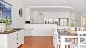 A modern kitchen with white cabinetry, a dining area with white chairs, and a large island with a sink.