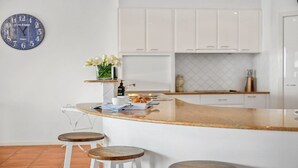 A modern kitchen with white cabinets, a curved island with stools, a clock, and a vase with flowers.