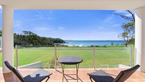 A balcony with two wicker chairs and a small table, overlooking a grassy area and the ocean.
