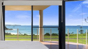 A room with a large glass door leading to a balcony with a view of the ocean and a distant island.