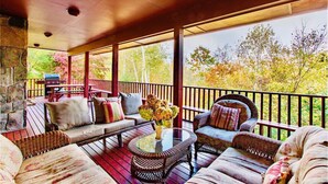 A covered outdoor seating area with wicker furniture, a round table, and a stone wall. - Family Reunion Gem!  Pool, Tennis, Deck, Fireplace, Views, Privacy - Dogs loved (Manchester)