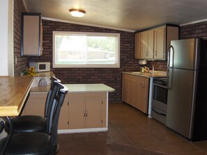 A kitchen with a wooden island, a refrigerator, cabinets, and a window. - Zion National Park Views House on Private Lot. No Cleaning Fee! (Virgin)