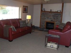 A living room with a red leather sofa, a fireplace, a small table, and a lamp. - Zion National Park Views House on Private Lot. No Cleaning Fee! (Virgin)