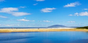 Een strand met kalm water, een heldere lucht en een berg in de verte.