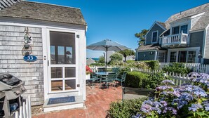 A house with a number 33 sign, a patio with chairs and an umbrella, and a white picket fence. - New Seabury Beach Cottage with stunning ocean views, steps to private beach (Mashpee)