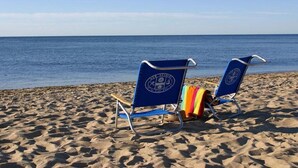 Two blue beach chairs with a colorful towel and a logo on the backrest, placed on a sandy beach with the ocean in the background. - New Seabury Beach Cottage with stunning ocean views, steps to private beach (Mashpee)