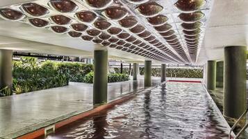 Swimmers enjoy the pool surrounded by a low, tiled edge and large columns, with a unique ceiling design creating a pattern on the floor.
