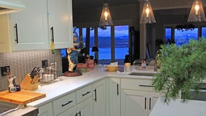 Una cocina moderna con armarios blancos, una estufa de acero inoxidable y un amplio ventanal con vista al agua.
