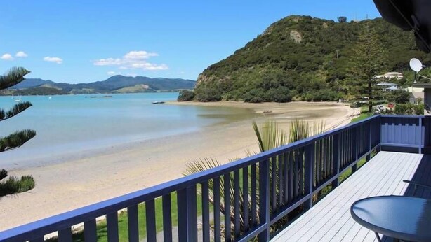 A balcony with a view of a beach and a hill. - Beachfront Bliss ~ Upper Deck Apartment (Coromandel Township)