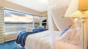 A bedroom with a large window offering a scenic view of the sea and mountains. - Beachfront Bliss ~ Upper Deck Apartment (Coromandel Township)