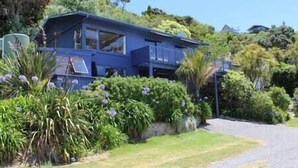 A two-story house with a balcony, surrounded by lush greenery and a clear sky. - Beachfront Bliss ~ Upper Deck Apartment (Coromandel Township)