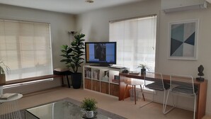 Ein modernes Wohnzimmer mit Glastisch, Fernseher, Bücherregal und Essbereich mit Stühlen.