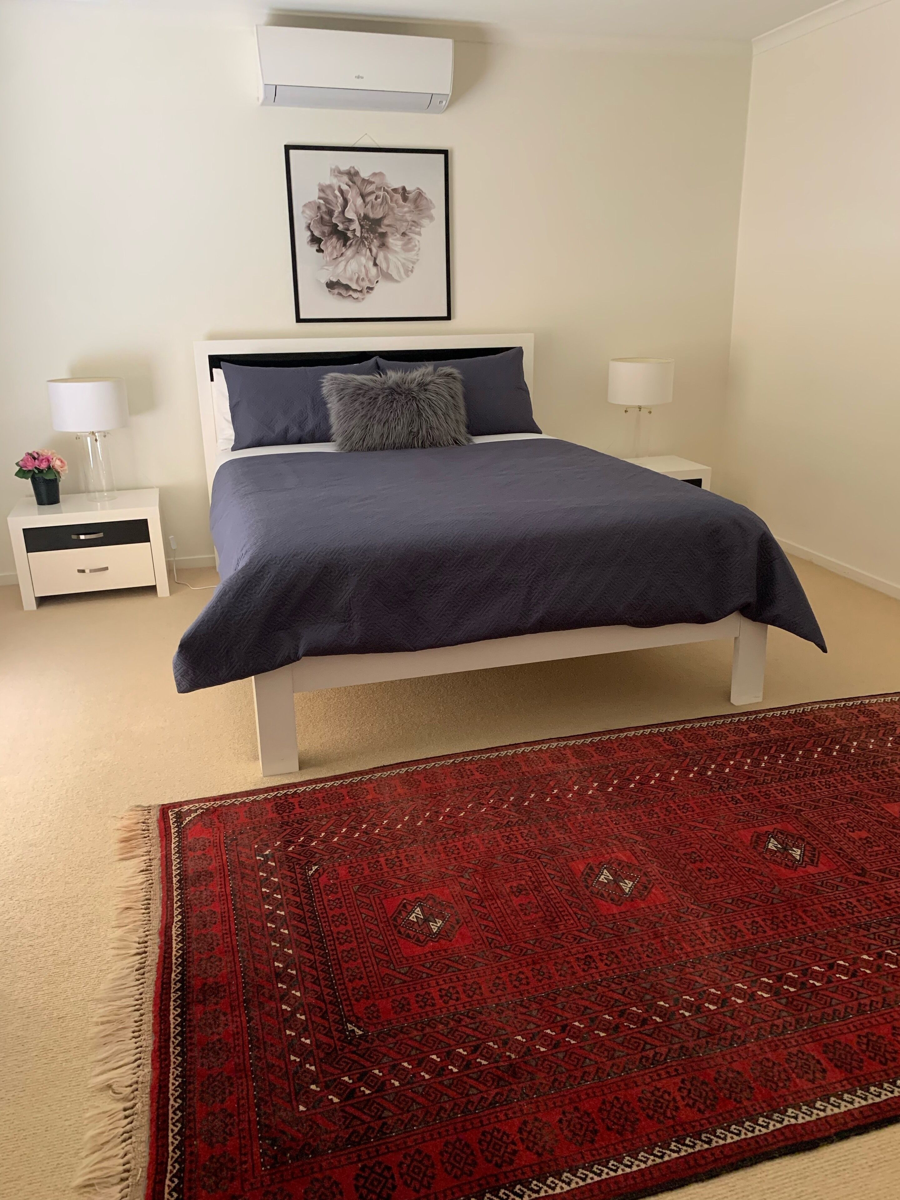 Une chambre à coucher avec un lit, des tables de chevet, un tapis rouge à motifs et un climatiseur au plafond.