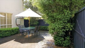 Eine Terrassengaststätte mit Tisch und Stühlen, einem weißen Sonnenschirm und einem Boden aus Ziegelsteinen.