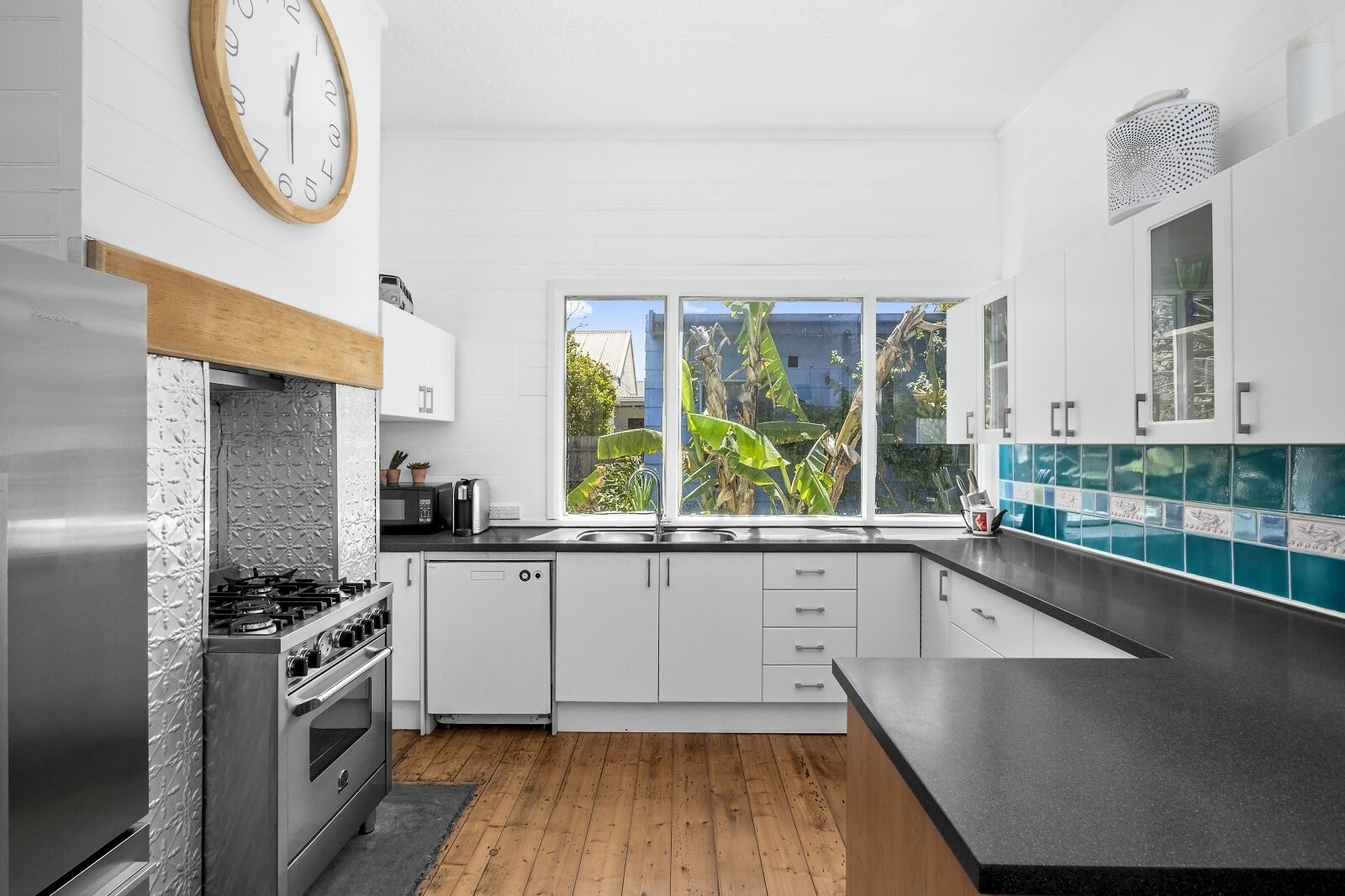 A modern kitchen with white cabinets, a stainless steel range, and a large window with a view of greenery.