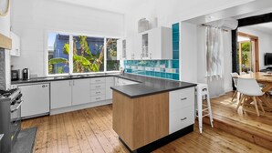 A modern kitchen with white cabinets, a wooden island, and a view of greenery outside.