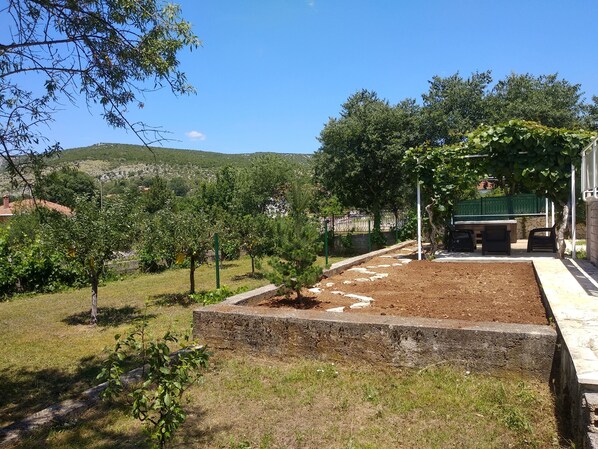 A garden with a paved area, trees, and a view of a hilly landscape.