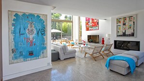 Un salon moderne agrémenté d’un grand tableau abstrait, d’une cheminée et d’un coin salon offrant une vue sur l’extérieur.