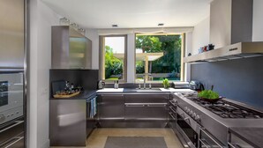 Une cuisine moderne dotée d’appareils électroménagers en acier inoxydable, d’une grande fenêtre et offrant une vue sur la verdure environnante.