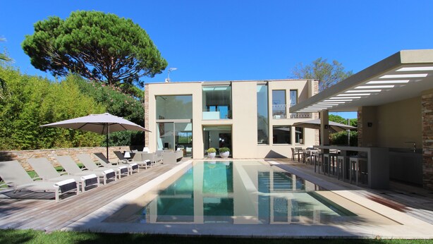 Une maison moderne dotée d’une piscine, d’un espace salon extérieur et d’un grand arbre.