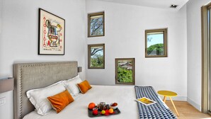 Une chambre d’hôtel moderne avec un grand lit, une table de chevet, une petite table ronde et une vue sur la verdure par les fenêtres.