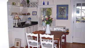 Una cocina con muebles blancos, una mesa de comedor de madera y sillas. Hay un jarrón con flores sobre la mesa, y un reloj en la pared.