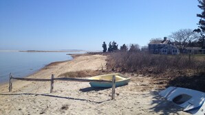 Una playa arenosa con un barco pequeño y una casa al fondo.