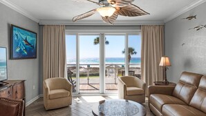 A room with a ceiling fan, a large window with a view of the beach, a sofa, a chair, and a small table. - 104 Sterling Sands Oceanfront Paradise Found! Steps to the Beach! (Destin)