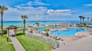 A pool area with a view of the beach, surrounded by palm trees and beach umbrellas. - 104 Sterling Sands Oceanfront Paradise Found! Steps to the Beach! (Destin)