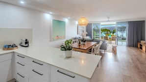 Una cocina moderna con armarios blancos y una isla de madera, un comedor con mesa y sillas, y vistas al exterior a través de ventanas amplias.