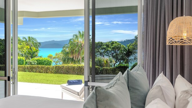 Un dormitorio con un amplio ventanal que ofrece vistas a un paisaje tropical y al mar.