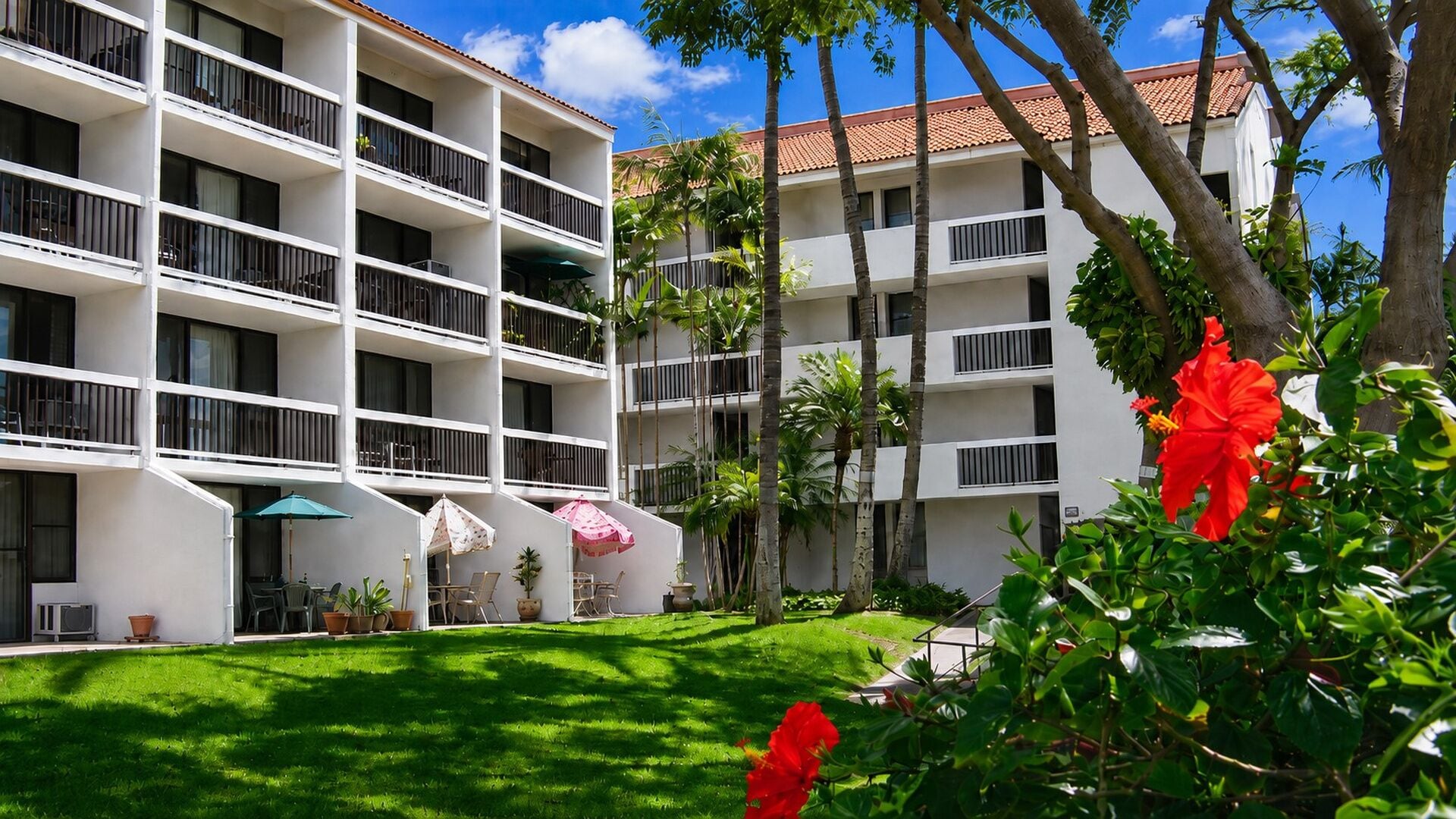 Un hôtel à plusieurs étages doté de balcons, d’une pelouse bien entretenue et de plantes tropicales.