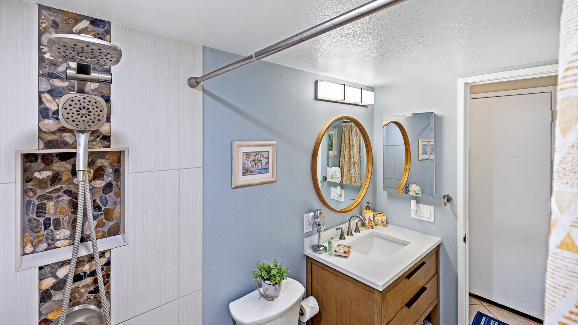 A bathroom with a stone shower enclosure, a wooden vanity with a sink, and two mirrors.