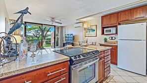 A kitchen with a gas stove, oven, microwave, and refrigerator. There is a dining area with a table and chairs, and a view of the outdoors.