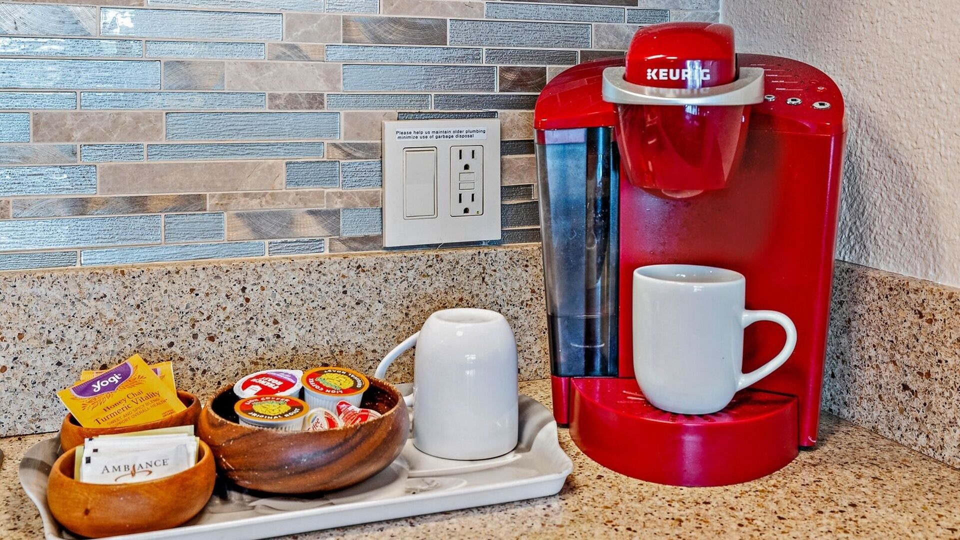 Une machine à café à l’extérieur rouge, une tasse blanche et un plateau avec un bol et des sachets de thé.