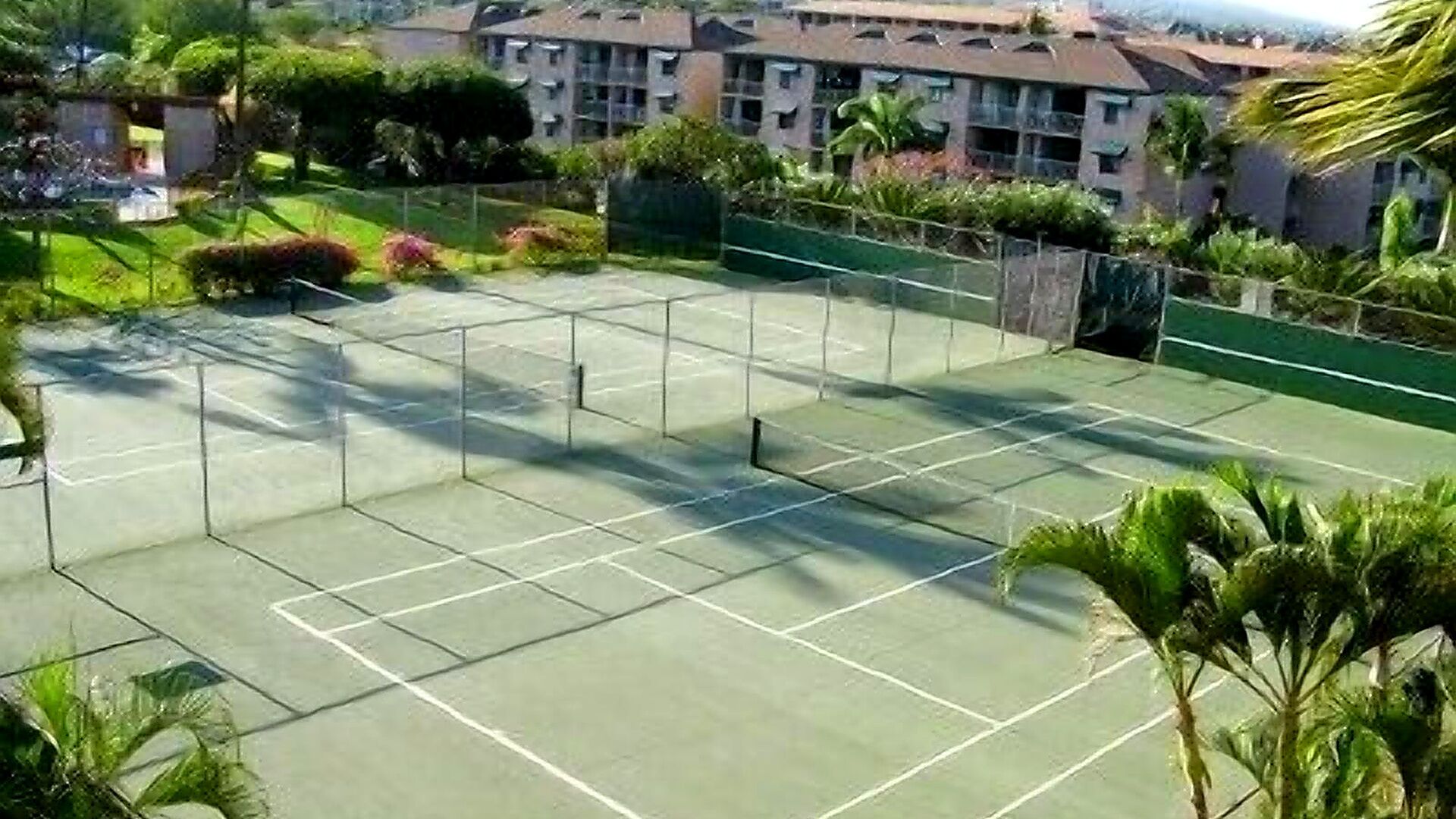 A tennis court surrounded by greenery and buildings.