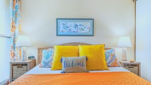 Una cama con dos almohadas amarillas, un cabecero tejido y una obra de arte enmarcada encima.